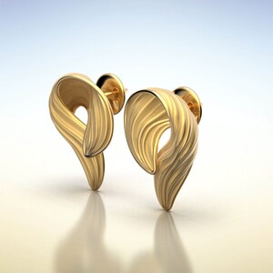 Puede incluir: Un par de pendientes de color dorado con un dise&ntilde;o &uacute;nico y abstracto. Los pendientes est&aacute;n hechos de un metal liso y texturizado y tienen una forma ligeramente curvada.