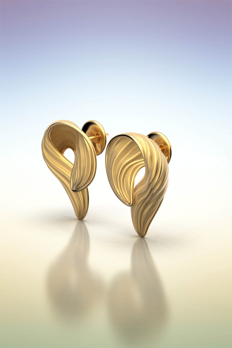 Puede incluir: Un par de pendientes de color dorado con un dise&ntilde;o &uacute;nico y abstracto. Los pendientes est&aacute;n hechos de un metal liso y texturizado y tienen una forma ligeramente curvada.