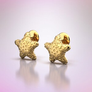 May include: A pair of gold star-shaped earrings with a textured surface.