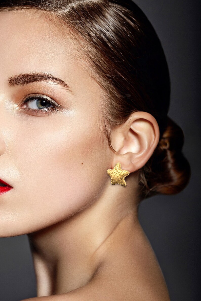 May include: A close-up of a woman's face with a gold star-shaped earring. The earring is textured and has a detailed design.