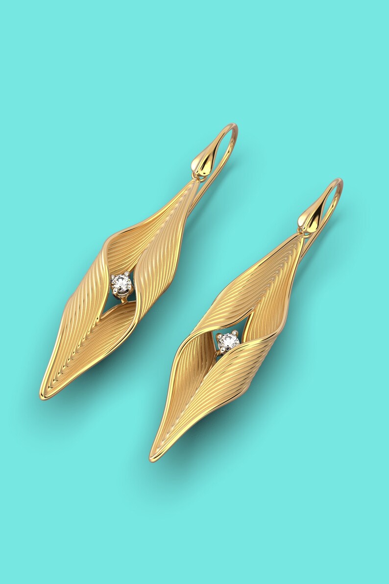 Puede incluir: Un par de pendientes de oro con un diamante en el centro de cada pendiente. Los pendientes tienen forma de hoja y una superficie texturizada.