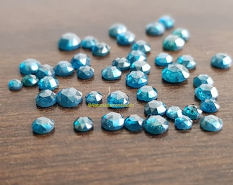 May include: A collection of loose blue diamonds, some with a more green hue, scattered on a brown wooden surface.  @Naturaldiamondstudio
