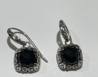 May include: A pair of silver earrings with black gemstone accents. The earrings feature a square-shaped gemstone set in a detailed silver frame. The earrings hang from a twisted silver wire.