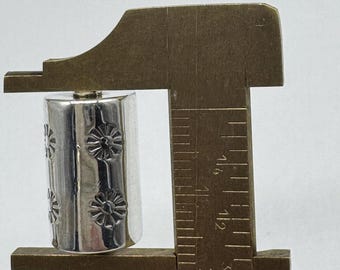 May include: A silver metal bead with a floral design is measured with a caliper. The bead is approximately 1.25 inches in length.