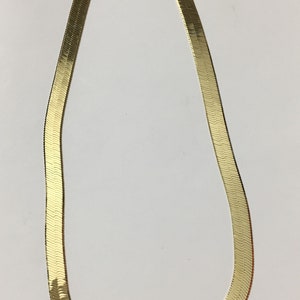 May include: A gold-tone snake chain necklace. The chain is made of a flat, textured metal and has a simple clasp.