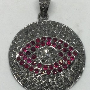 May include: A silver pendant with a black diamond and ruby eye design. The pendant is oval shaped and has a bail at the top for attaching to a chain.