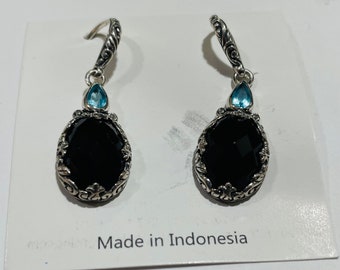 May include: A pair of silver dangle earrings with black oval-shaped stones and a small light blue stone at the top of each earring. The earrings are on a white background with the text "Made in Indonesia".