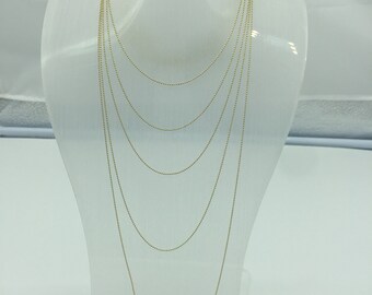 May include: A gold chain necklace on a white display stand. The chain is layered in multiple lengths.