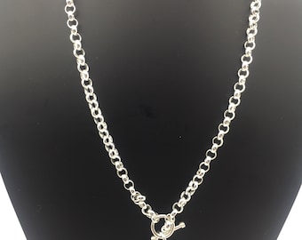 May include: A silver-toned necklace featuring a thick rolo chain and a toggle clasp closure. A smooth, heart-shaped pendant hangs from the center of the toggle mechanism. The heart pendant is partially covered by a small, clear protective plastic film.