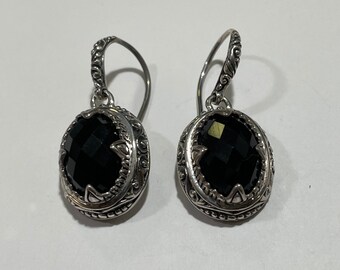 May include: A pair of silver dangle earrings with black gemstone accents. The earrings feature a detailed, ornate design.