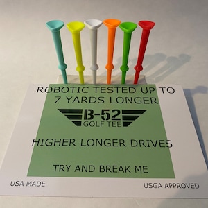 May include: A set of six golf tees in different colors, including teal, yellow, white, orange, green, and red. The tees are arranged in a row on a white surface with a green background. The background has the text "ROBOTIC TESTED UP TO 7 YARDS LONGER", "B-52 GOLF TEE", "HIGHER LONGER DRIVES", "TRY AND BREAK ME", "USA MADE", and "USGA APPROVED".