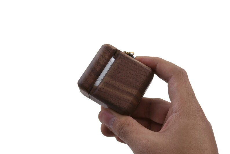 May include: A dark brown wooden case with a gold clasp and a black strap. The case is designed to hold small items like earbuds or jewelry.