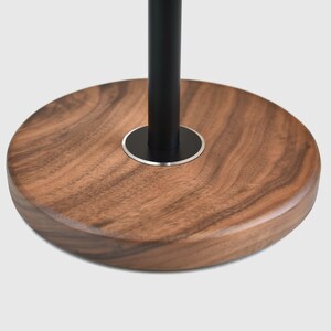 May include: A round wooden base with a black metal pole extending from the center. The base is made of dark wood with a natural grain pattern.