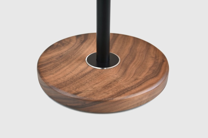 May include: A round wooden base with a black metal pole extending from the center. The base is made of dark wood with a natural grain pattern.