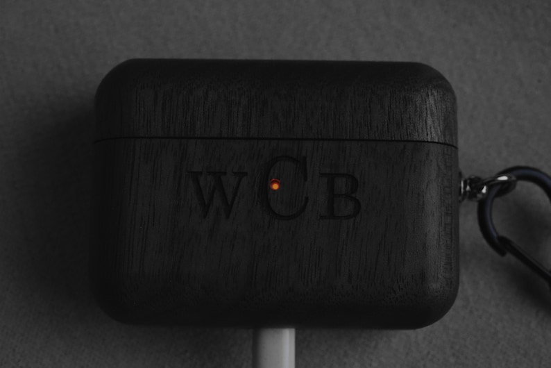 May include: Black wooden case with a carabiner clip and the initials "WCB" engraved on the front. A small orange light is visible on the case.