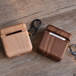 May include: Two wooden cases for Airpods, one made of light wood and the other of dark wood, both with a metal carabiner clip.