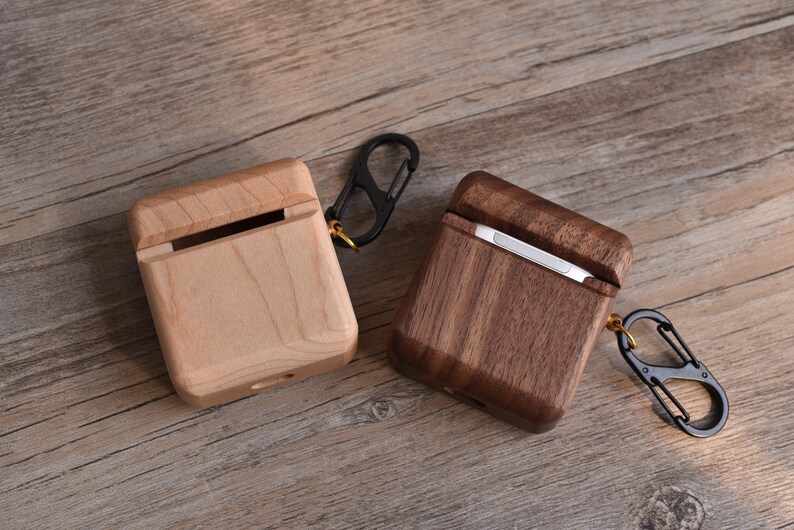 May include: Two wooden cases for Airpods, one made of light wood and the other of dark wood, both with a metal carabiner clip.