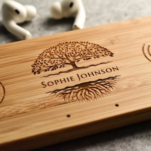 Pode incluir: Uma base de carregamento sem fios de madeira com um design de árvore e raízes. O texto "Sophie Johnson" está gravado na base. A base tem dois pontos de carregamento sem fios, indicados por símbolos de raios.