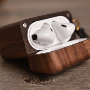 May include: A wooden case with a dark brown walnut finish, open to reveal two white wireless earbuds inside.