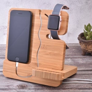 May include: A wooden charging stand with a phone holder, a watch holder, and a space for a charging cable. The stand is made of light brown bamboo wood.