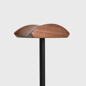 May include: A wooden headrest with a curved shape, mounted on a black metal pole. The headrest is made of dark brown wood and has a smooth finish.