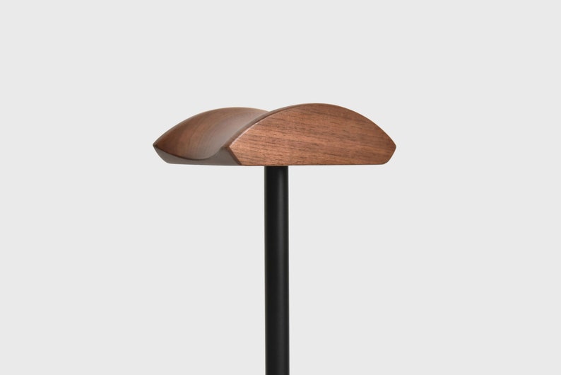 May include: A wooden headrest with a curved shape, mounted on a black metal pole. The headrest is made of dark brown wood and has a smooth finish.