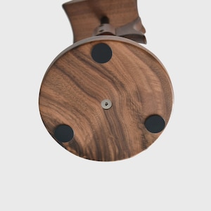 May include: A wooden stand with a round base and four black rubber feet. The stand is made of dark wood with a natural grain pattern.