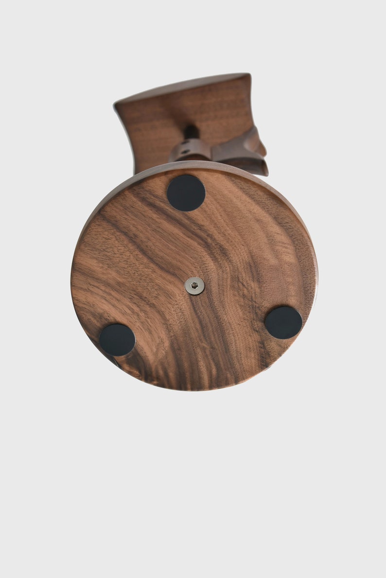 May include: A wooden stand with a round base and four black rubber feet. The stand is made of dark wood with a natural grain pattern.