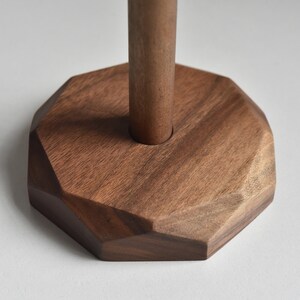 May include: A wooden base with a geometric shape and a round hole in the center. The base is made of dark brown wood.