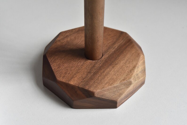 May include: A wooden base with a geometric shape and a round hole in the center. The base is made of dark brown wood.