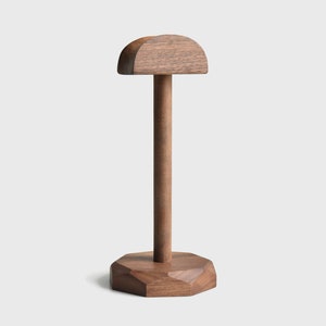 May include: A wooden headphone stand with a rounded top and a geometric base. The stand is made of dark brown wood.