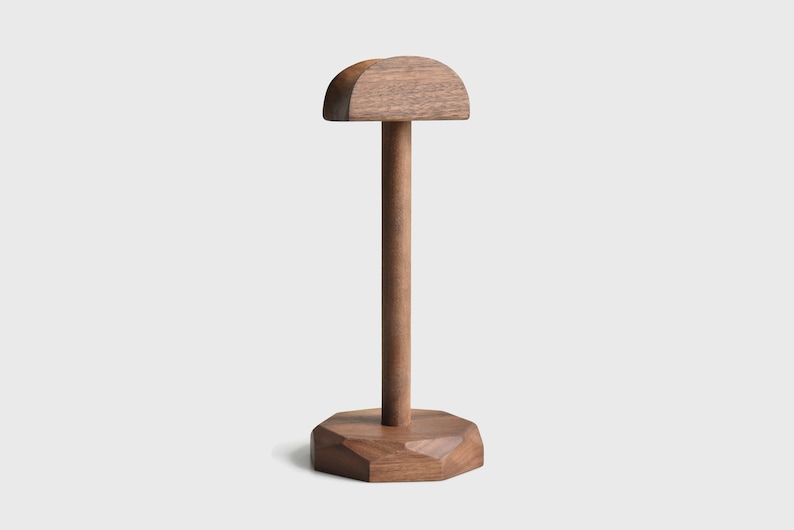 May include: A wooden headphone stand with a rounded top and a geometric base. The stand is made of dark brown wood.