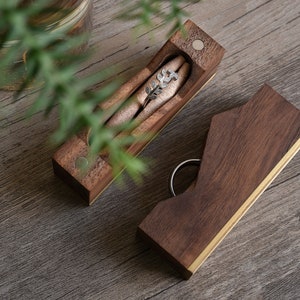 May include: Two wooden ring boxes with a gold trim. The top box is open and has a small silver ring inside. The bottom box is closed.