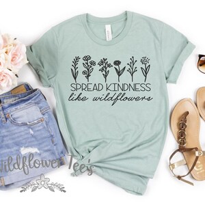 May include: A light green t-shirt with the text "SPREAD KINDNESS like wildflowers" and a floral design. The shirt is paired with denim shorts, sunglasses, and sandals. A bouquet of pink roses is also included.