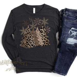 May include: A long-sleeved, dark grey t-shirt with a design of three Christmas trees. The trees are decorated with a leopard print and gold glitter. The design is surrounded by snowflakes.