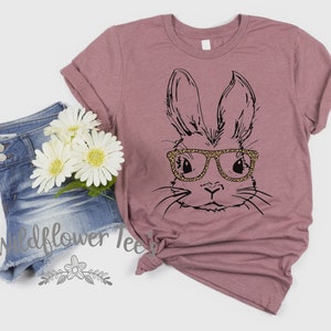 May include: A mauve t-shirt with a black and white illustration of a bunny wearing leopard print glasses. The bunny is looking directly at the viewer. The t-shirt is on a white background.