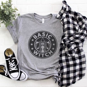 May include: A gray t-shirt with a black and white graphic of a witch with a witch hat and the text "BASIC WITCH" in a circle.