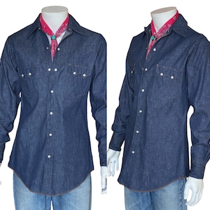 May include: A dark blue denim shirt with a long sleeve and a button-down collar. The shirt has two chest pockets with button closures and a red bandana tied around the collar.