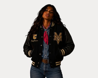 Op de afbeelding: Zwarte varsity jas met gouden en witte accenten. Voorzien van een groot "M" en "C" embleem met tekst. De jas heeft een knoopsluiting, zwarte leren mouwen en gestreepte manchetten en zoom. Een roze sjaal wordt om de nek gedragen.