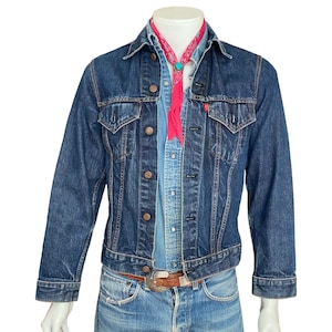 May include: A dark blue denim jacket with a red bandana tied around the collar. The jacket has a button-up front and multiple pockets.