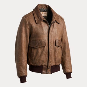 Puede incluir: Chaqueta bomber de cuero marrón con cremallera, dos bolsillos delanteros y un dobladillo y puños acanalados de color marrón oscuro. La chaqueta tiene un cuello clásico y una estética vintage.