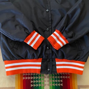 May include: Black bomber jacket with orange and white striped cuffs and waistband.