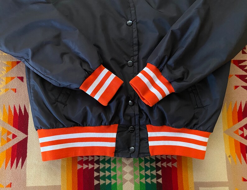 May include: Black bomber jacket with orange and white striped cuffs and waistband.