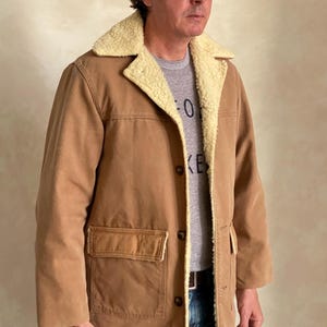 May include: A brown corduroy jacket with a sherpa lining and a single chest pocket. The jacket has a button closure and a corduroy collar.