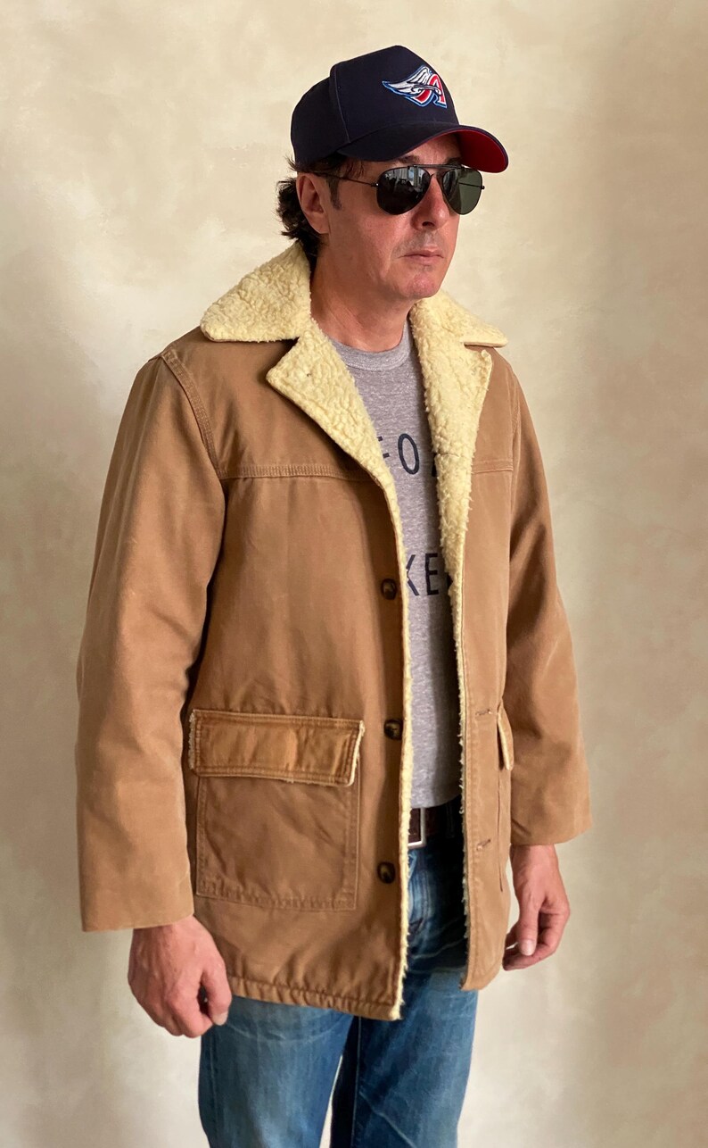 May include: A brown corduroy jacket with a sherpa lining and a single chest pocket. The jacket has a button closure and a corduroy collar.