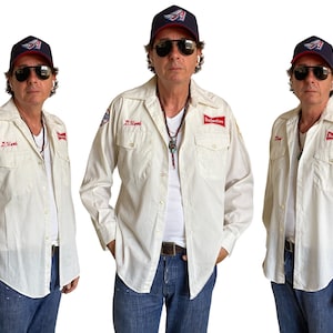 May include: Three images of a person wearing a white shirt with Budweiser patches and a baseball cap. The shirt has a name embroidered on the pocket. The person is wearing sunglasses and a necklace. The background is white.