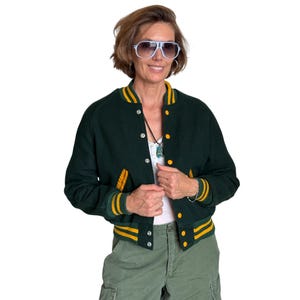 Peut inclure: Veste de style universitaire vert foncé avec des rayures jaunes et blanches sur les poignets, le col et les poches. La veste a une fermeture boutonnée et est portée avec un pantalon cargo vert.