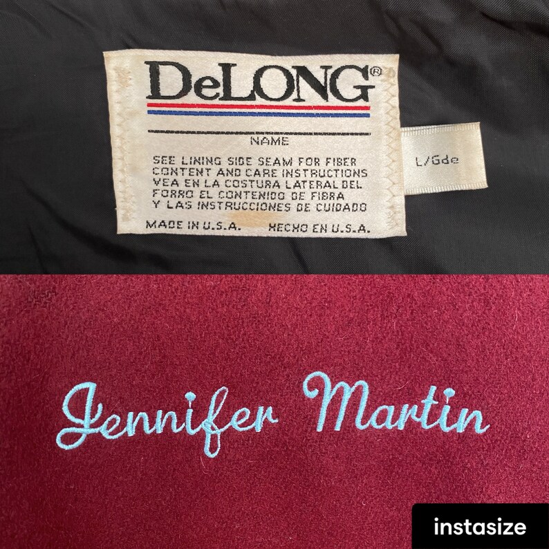 Op de afbeelding: Een close-up van een bordeauxrode jas met de naam "Jennifer Martin" geborduurd in lichtblauw garen. De binnenkant van de jas heeft een label met het merk "DeLONG" en wasvoorschriften. Het label vermeldt ook "Made in U.S.A."