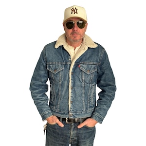 May include: A denim jacket with a cream-colored shearling lining and a matching baseball cap. The jacket has a classic design with buttoned pockets and a collar. The cap features a logo.