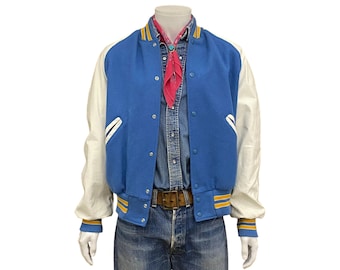 Op de afbeelding: Een blauw en wit varsity jack met gouden strepen op de mouwen. Het jack is gemaakt van wol en leer.